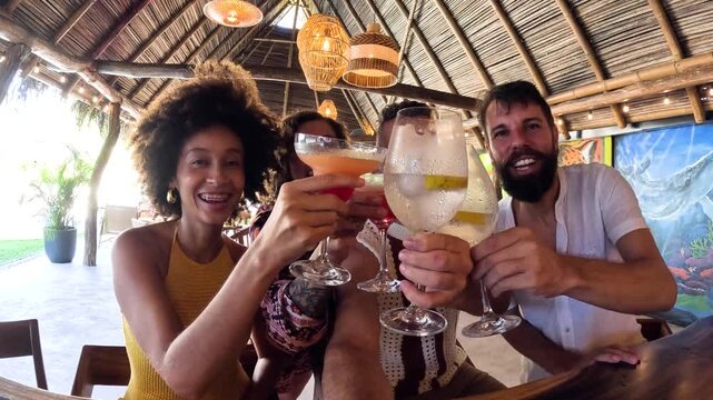 Diverse group of friends celebrating and clinking glasses with colorful cocktails. Happy people enjoying a party at a beach resort bar