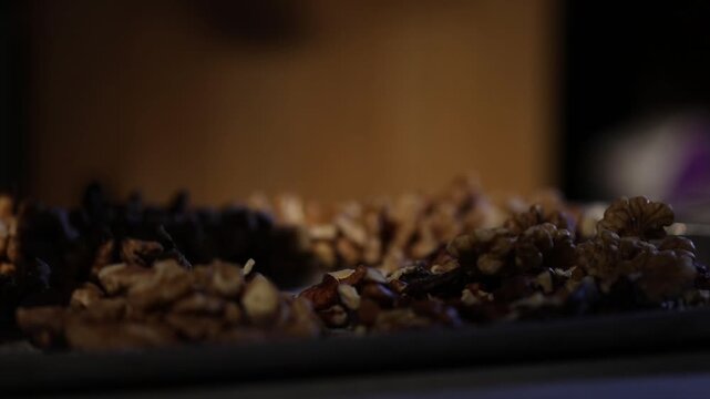 Close-up of hands stringing walnuts on thread for traditional Georgian dessert Churchkhela. Authentic homemade preparation process arranging nuts on a metal tray in a cozy kitchen setting.

