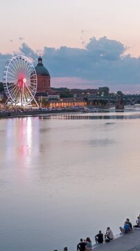 Aerial view of Port de la Daurade park along the Garonne River day to night transition timelapse in Toulouse, France. La Grave Hospital with Saint-Pierre Bridge after sunset with colorful clouds