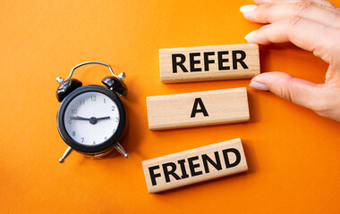 Refer a Friend symbol. Concept words Refer a Friend on wooden blocks. Businessman hand. Beautiful orange background with alarm clock. Business and Refer a Friend concept. Copy space.