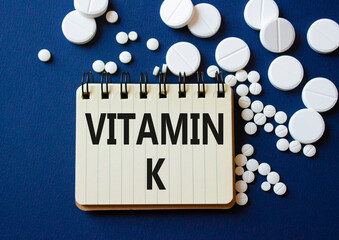 Vitamin K symbol. Concept word Vitamin K on notebook. Beautiful deep blue background with pills. Medicine and Vitamin K concept. Copy space