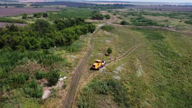 Aerial view of tractor with a cable drum laying fiber optic hawser at countryside. Workers guiding and adjusting rope to ensure proper placement under ground for communication or power infrastructure