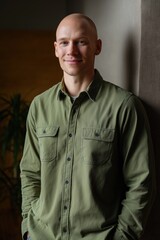 Confident bald caucasian young male in green shirt smiling indoors