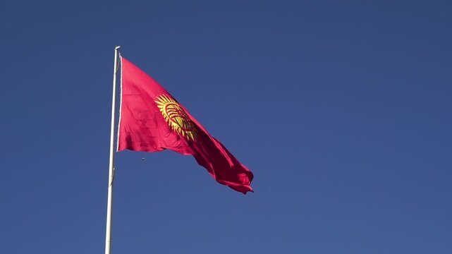 Red flag of Kyrgyzstan fluttering in the wind, featuring a golden sun with forty rays and a central tunduk emblem, symbolizing national identity, unity, and cultural heritage under a vibrant sky.