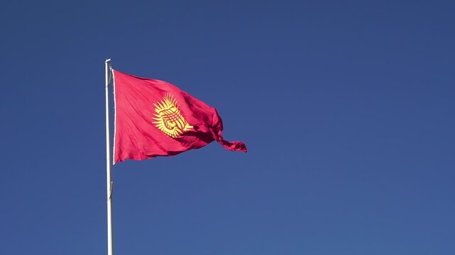 Red flag of Kyrgyzstan featuring a radiant yellow sun with forty rays and a tunduk emblem in the center, fluttering high on a pole, symbolizing national pride, unity, and cultural identity.