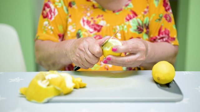 Senior woman hands peeling a fresh lemon with a knife