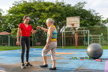 Active senior woman practicing balance exercises holding hands with female trainer outdoors