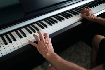 Close-up of the hands of an older man learning to play the piano at home