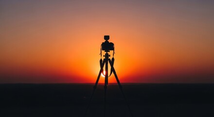 Camera on a tripod silhouetted against a vibrant orange sunset backdrop