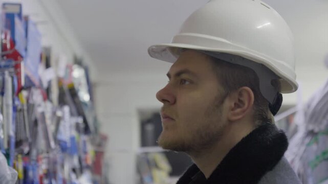 Man in a hard hat looking at tools on shelves in a hardware store.
