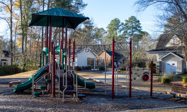 Empty Childrens Community Park Playground Structure with Green Slides Monkey Bars and Red Poles Resting on a Mulch Surface Surrounded by Suburban Homes and Autumn Trees