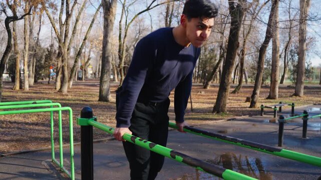 Man practicing street workout on parallel bars in sunny autumn park,