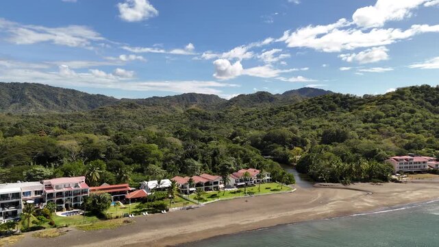 Aerial rising shot of Costa Rican beach front condos with palm trees and jungle river.
