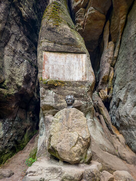 A bronze bust and commemorative plaque of Johann Wolfgang von Goethe from 1932 nestled within towering, mossy sandstone rock formations in the Czech Republic under soft natural light.