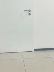 Minimalist detail of a white medical office door with metal handle on tiled floor