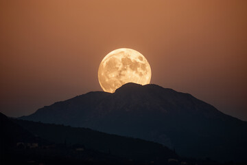 Full moon rising over silhouetted mountains at twilight