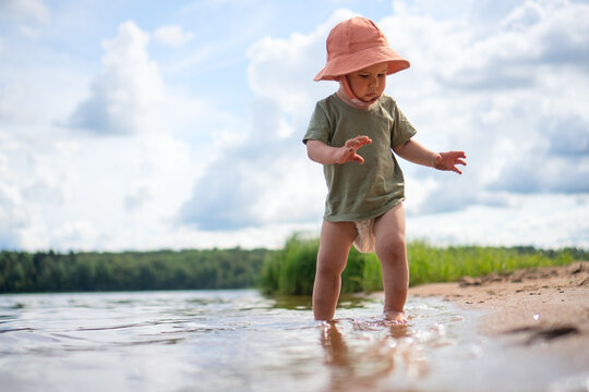 A toddler runs on the sandy beach with an orange hat, feeling the freedom and joy of movement.