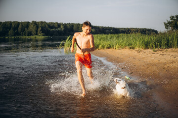 Boy and Dog Playing on Lakeside Beach with Stick