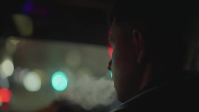 Man smokes inside car at night, Indoor car scene featuring man smoking with city lights background, Reflective scene where man smokes in vehicle illuminated by neon lights and shadows