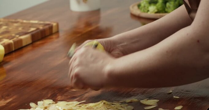 Close-up shot of hands peeling a fresh potato with a vegetable peeler on a wooden table. Home cooking process, preparing ingredients for a vegan meal, healthy food concept, rustic kitchen and natural