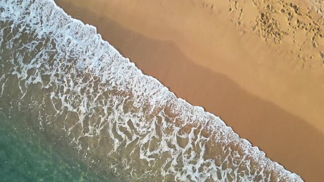 Cenital aerial drone view of sea waves crashing on the shore, sand and foam on the coastline, 4k nature background