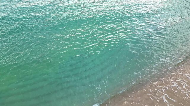 Cenital aerial drone view of sea waves crashing on the shore, sand and foam on the coastline, 4k nature background