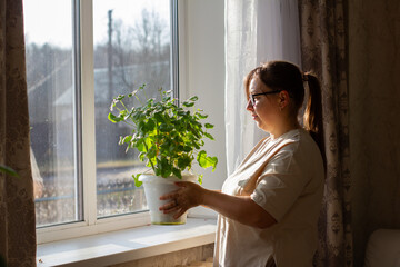A woman stands by a sunny window, carefully placing a potted houseplant on the sill to allow it to receive natural light. The woman encourages the healthy growth and development of the houseplant.