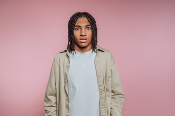 Fototapeta premium Person with braided hair stands against a pink background looking surprised or confused while wearing a casual outfit
