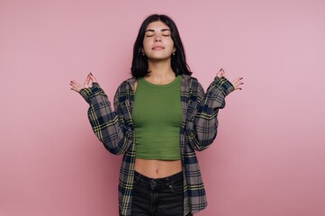 Young woman poses with closed eyes and relaxed posture against a plain pink background, wearing a...
