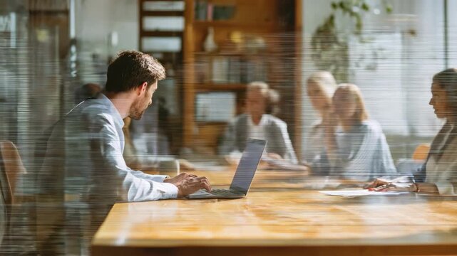 Medium shot of a hybrid legal deposition showing a lawyer at a desk engaging with colleagues on a laptop blending digital and physical presence.
