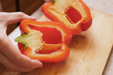 Cook shows a halved sweet red pepper on a cutting board, ready to remove seeds and slice, illustrating step by step tutorial stuffed pepper recipes in culinary courses and food blogs