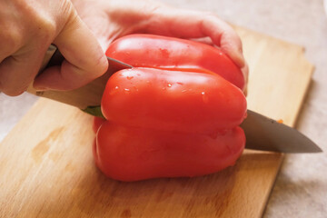 Cook shows a halved sweet red pepper on a cutting board, ready to remove seeds and slice, illustrating step by step tutorial stuffed pepper recipes in culinary courses and food blogs