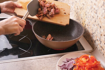Home cook slides marinated meat pieces from a wooden cutting board into a preheated wok on the stove, first step of cooking a hot stir fry or stew, ideal for recipe videos