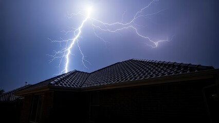 Dramatic view of a powerful electrical lightning discharge illuminating the dark purple sky above a residential home roof.