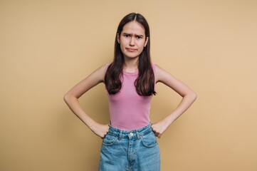 Obraz premium Expression of concern from a young girl with hands on hips in front of a plain background during daytime