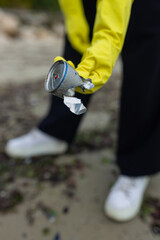 volunteer picking up a crushed metal can during beach cleanup, highlighting pollution, waste problem, ecology, coastal protection and environmental awareness.