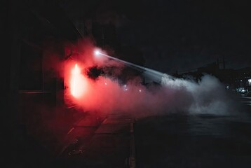 Obraz premium Red smoke and a piercing white light beam illuminating a mysterious urban night scene