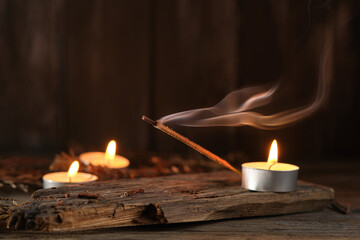 Incense Stick Releases Smoke Next to Candles on Wooden Surface at Night
