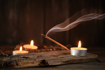Incense Stick Releases Smoke Next to Candles on Wooden Surface at Night