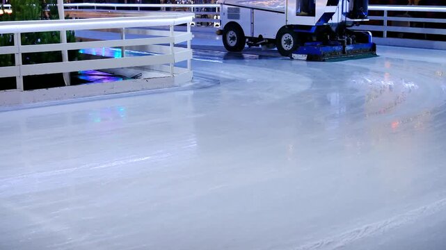 Large ice resurfacing machine maintaining a smooth surface on a bright ice rink with white fence