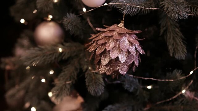 Sparkling rose gold pinecone ornament hanging on a festive green Christmas tree branch with warm glowing lights