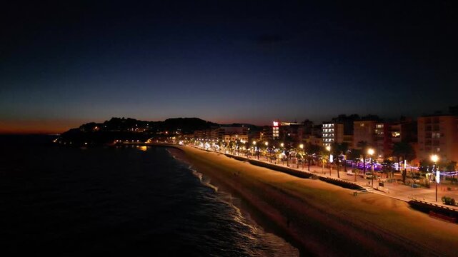 Aerial drone view of coastline town at night, moonlight reflected on sea waves, city lights, vertical background