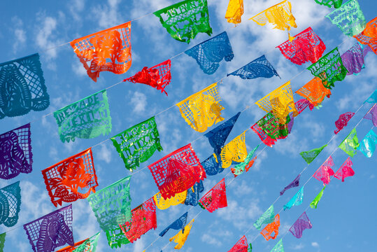 Festive garlands of colorful cut-out paper hung as decoration against a blue sky. Papel picado.