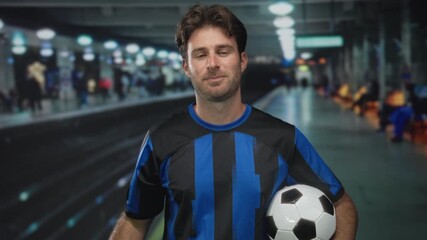 Man smiling holds money bag by rope and cradles soccer ball under arm in station building; confidence success reward. - Powered by Adobe