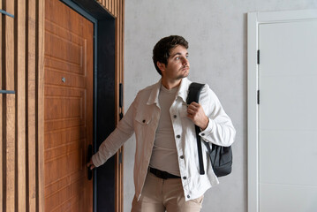 Young man entering apartment through wooden door