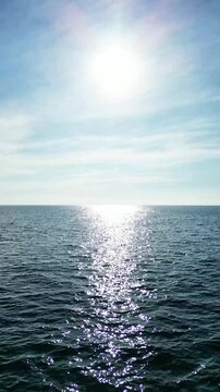 Aerial drone view, flying over the blue sea waves towards the sun, water reflection, vertical background