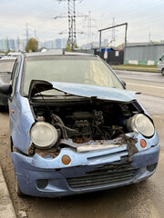 Old Neglected Vehicle Scene, Rusty Compact Vehicle With Broken Signals And Deflated Tire, Dilapidated Blue Hatchback Neglected Outside With Damaged Front And Worn Appearance