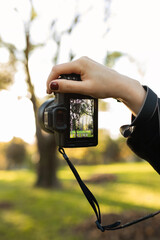 Close-up of a digital camera held up by a hand outdoors, with soft bokeh background in a green park. Photography equipment in natural light, creative shooting moment. © руслан малыш