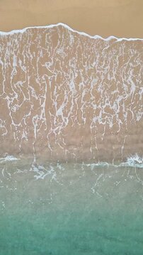 Cenital aerial drone view of sea waves crashing on the shore, sand and foam on the coastline, vertical nature background