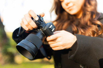 Close-up of a young woman holding a digital camera while photographing outdoors in warm sunlight. Soft golden-hour light, creative lifestyle photography moment.